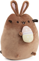 brown cuddly stuffed animal cat name Pusheen with bunny ears and holding an easter egg